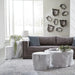 A styled living room featuring a gray fabric sofa, three organic-shaped white tree-stump coffee tables, a gray rug, and a wall-mounted cluster of starburst wall art.