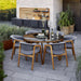 Boxhill's Luna Outdoor Dining Armchair Lifestyle image with teak round table with glass top at patio