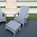 A light gray outdoor patio set featuring an Adirondack chair, a matching ottoman, and part of a second chair, placed on a dark patio surface with white steps and green grass in the background.