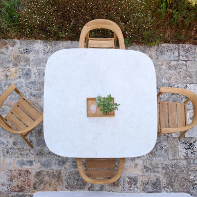 Top view of a white square dining table paired with four wooden outdoor armchairs on a patio