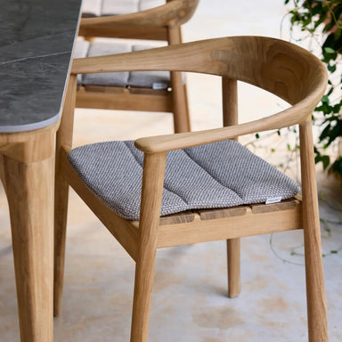 Wooden outdoor dining armchair with gray seat cushion set beside a dining table on a patio