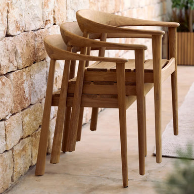 Stackable wooden patio dining armchairs stacked together against a stone wall
