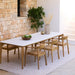 Rectangular outdoor dining table paired with six teak outdoor dining chairs with arms on a patio