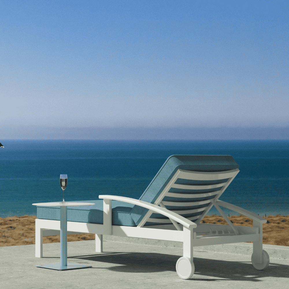 Modern outdoor chaise lounge with aluminum frame and blue-green cushions, accompanied by a small side table on a concrete floor, with sea view