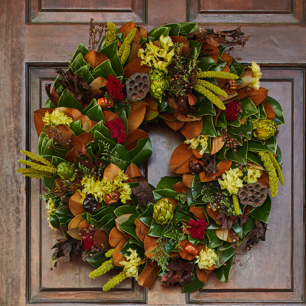 A vibrant autumn wreath of magnolia, dried leaves, and yellow accents on a rustic wooden door, celebrating the season's bounty.