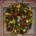 A vibrant autumn wreath of magnolia, dried leaves, and yellow accents on a rustic wooden door, celebrating the season's bounty.