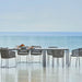 Boxhill's Moments Stackable Arm Chair lifestyle image with dining table at seafront