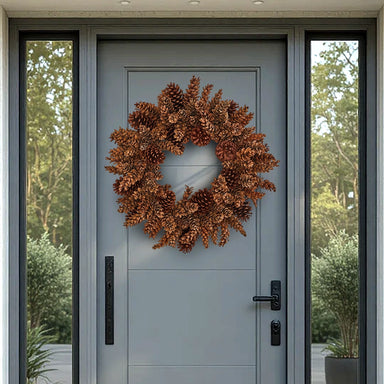 Brown natural pinecone wreath on a gray front door with side glass panels.