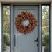 Brown natural pinecone wreath on a gray front door with side glass panels.