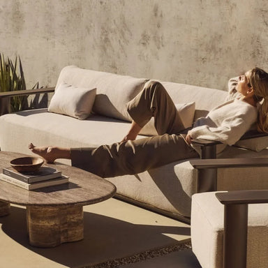Rectangular aluminum sofa brown with cushioned seating, woman relaxing comfortably against a plain wall