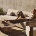 Rectangular aluminum sofa brown with cushioned seating, woman relaxing comfortably against a plain wall