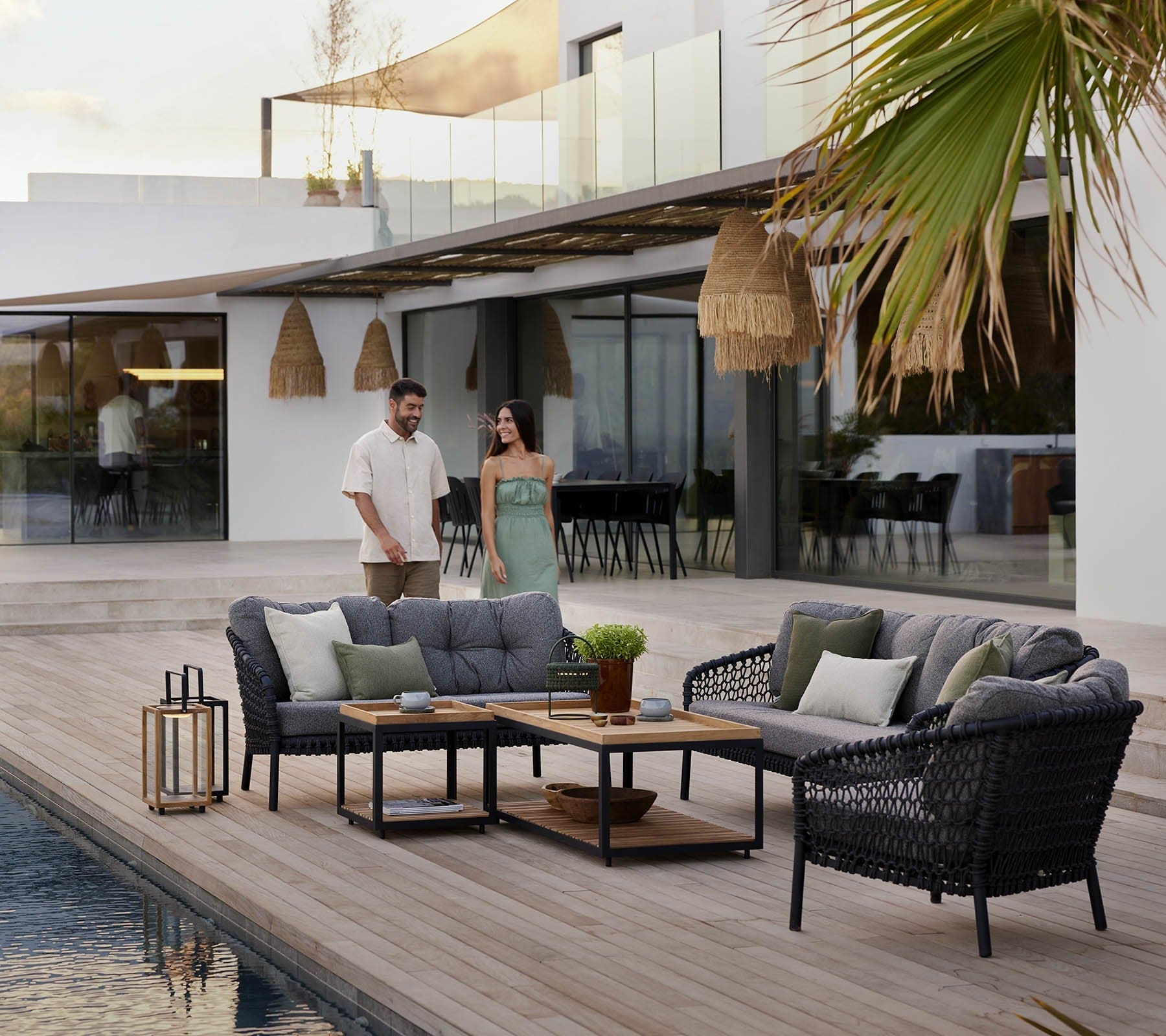 Boxhill's Ocean Large Outdoor 2-Seater Sofa lifestyle image beside the pool with other Ocean Sofa and Chair Collection, Level Coffee Table with Teak Top and 2 people walking