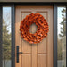 Orange lacquer wreath hanging on a light brown wooden front door with black frame and glass side panels.