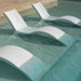 Three modern curved white outdoor lounge chairs partially submerged in a swimming pool with clear turquoise water.