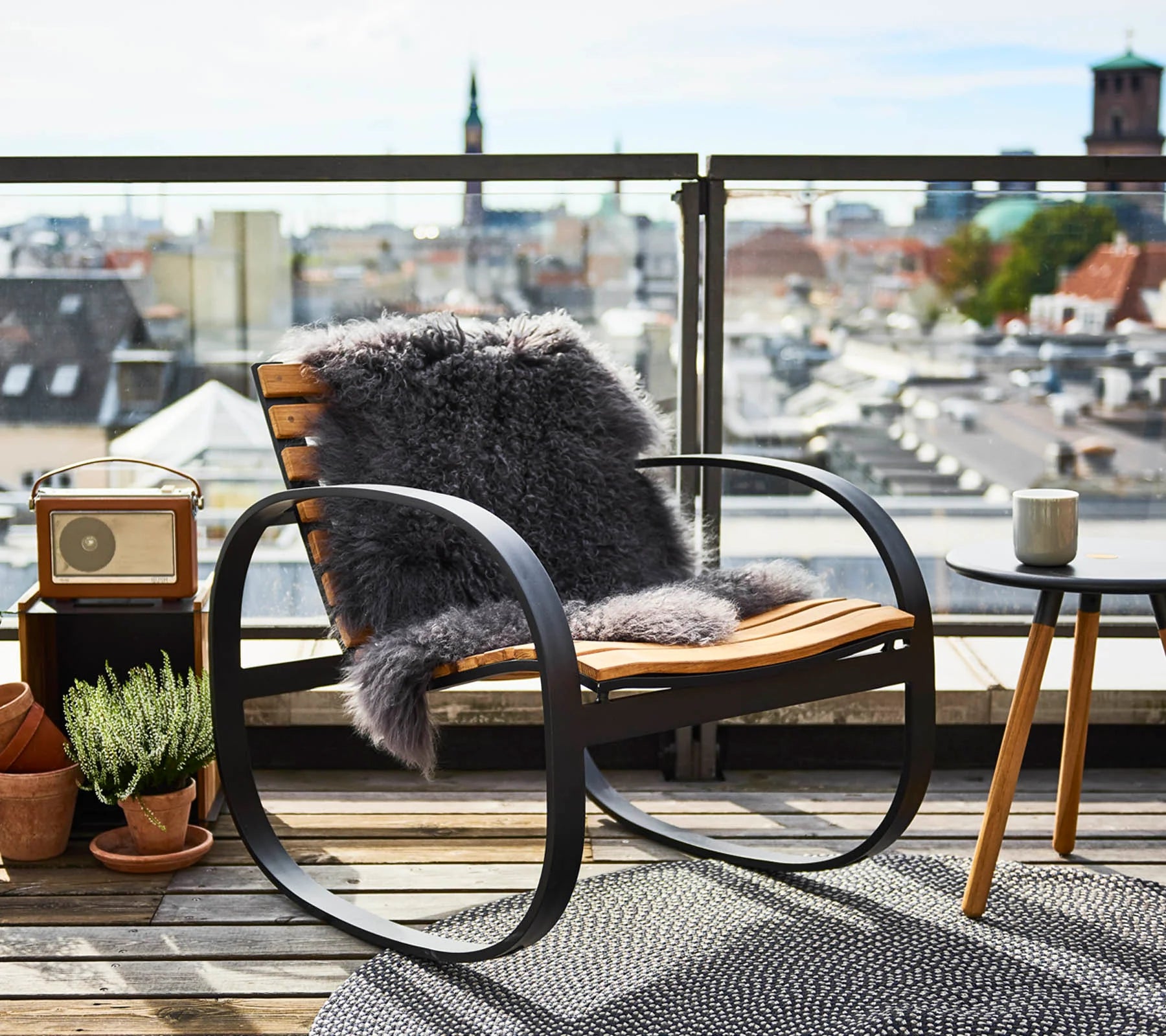 Boxhill's Parc teak outdoor rocking chair with a dark grey fabric on it and outdoor round side table with a cup on it placed on balcony