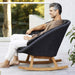  Boxhill's Peacock dark grey outdoor rocking chair with teak base with a man sitting on it wearing a brown shirt