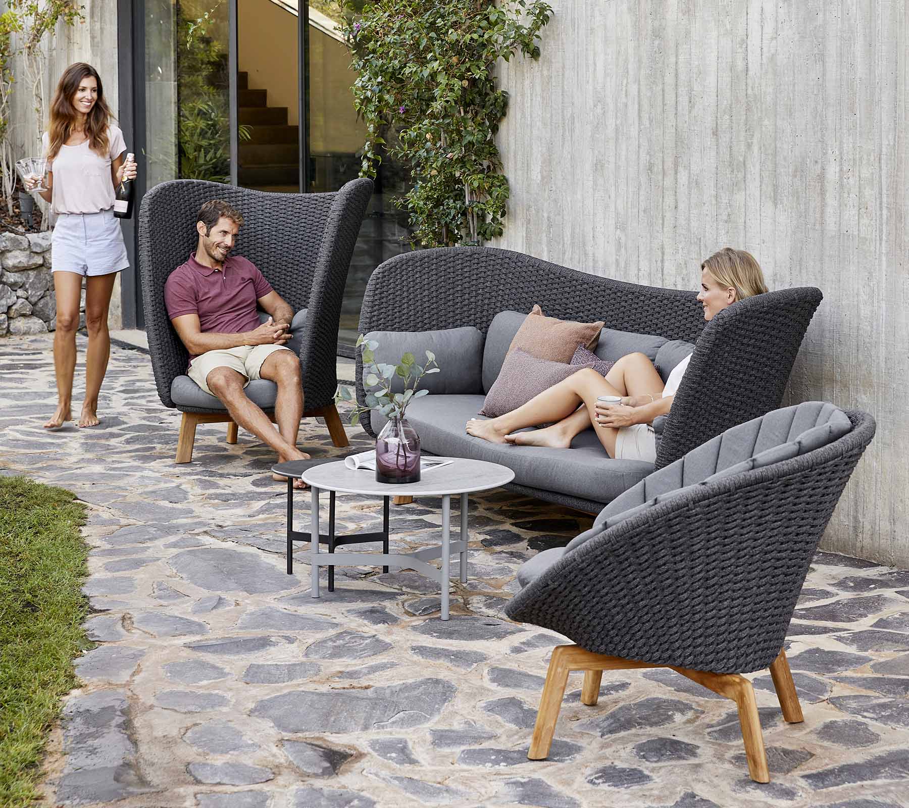  Boxhill's Peacock dark grey outdoor wing highback chair with a man sitting on it  having a chat to a woman sitting on the outdoor sofa