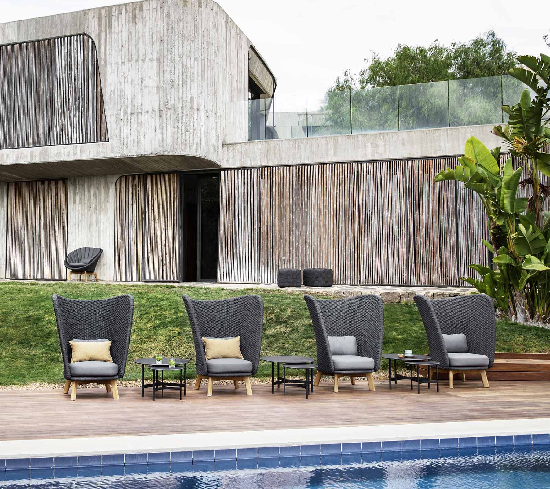 Boxhill's Peacock dark grey outdoor wing highback chair with small dark grey round table in a row placed beside the pool