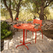 Orange round aluminum outdoor cafe table paired with a matching dining chair set on a stone patio surrounded by greenery
