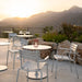  White round aluminum outdoor cafe tables and chairs with table lanterns set on a patio with a view of a distant hills
