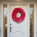 Decorative bright red-pink lacquer wreath on a white front door with glass panels.