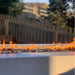 Close up view of a gray outdoor rectangular metal powdered coated fire pit table with flames over lava rocks