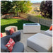 A white outdoor rectangular metal powdered coated fire pit table set on an outdoor patio with two gray chairs and a large white ottoman