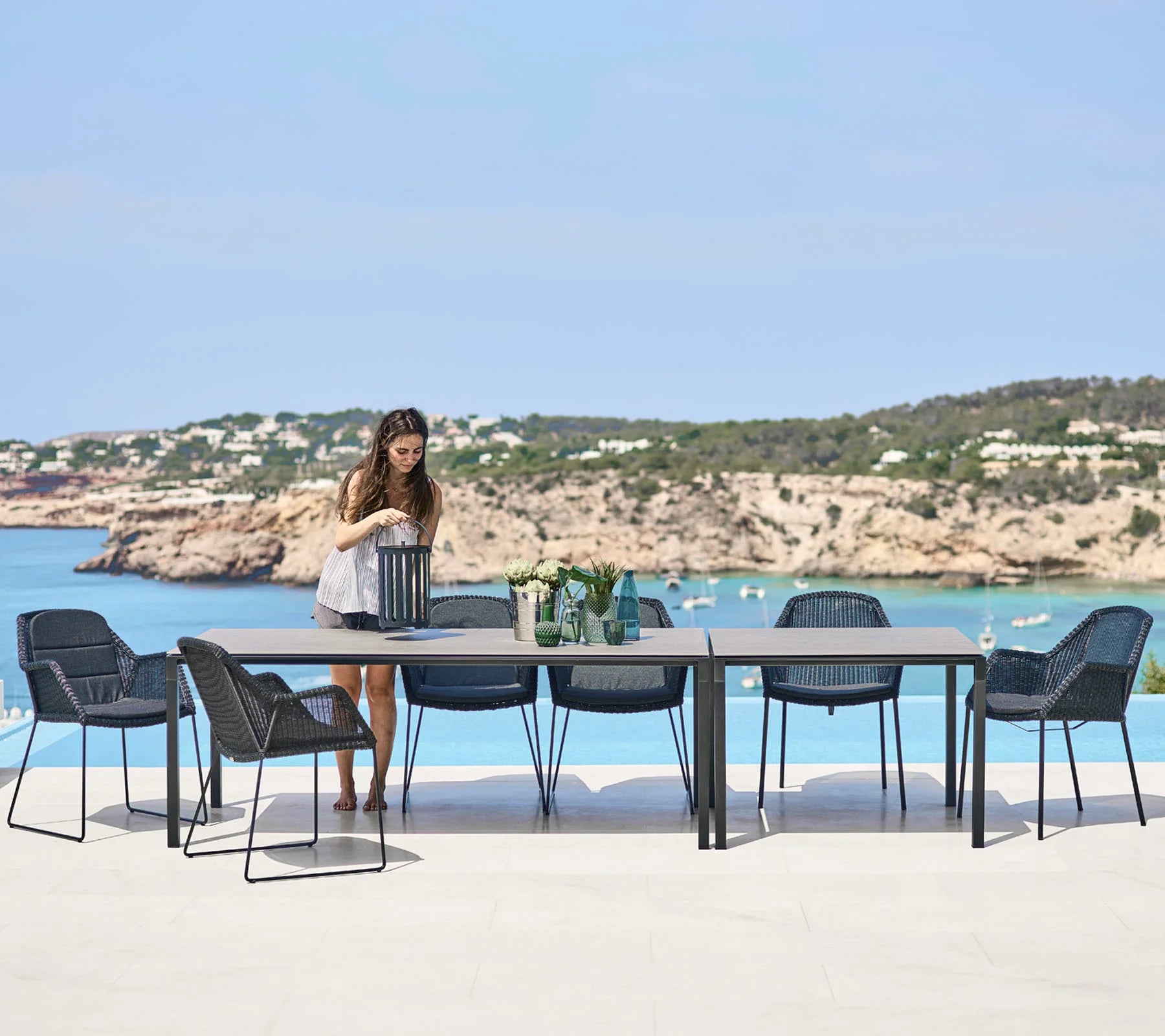 Boxhill's Pure lava grey aluminum outdoor dining table with black outdoor dining chairs and a woman holding a black lantern