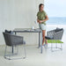 Boxhill's Pure light grey aluminum outdoor dining table with grey outdoor dining chairs and a woman in green shirt standing