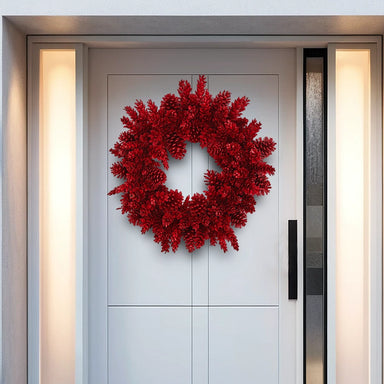 Red pinecone holiday wreath displayed on a modern white front door with glass side panels.