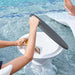 A person using a dark gray swim seat cushion on a white pool seat in a swimming pool, with water splashing around it.