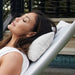 A woman reclining on a white outdoor lounge chair beside a swimming pool, with a white textured pillow supporting her head.
