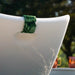 A close-up of a white LEDCE outdoor bathtub or tub shell with a green patterned fabric strap attached near the rim, photographed outdoors with blurred trees in the background.
