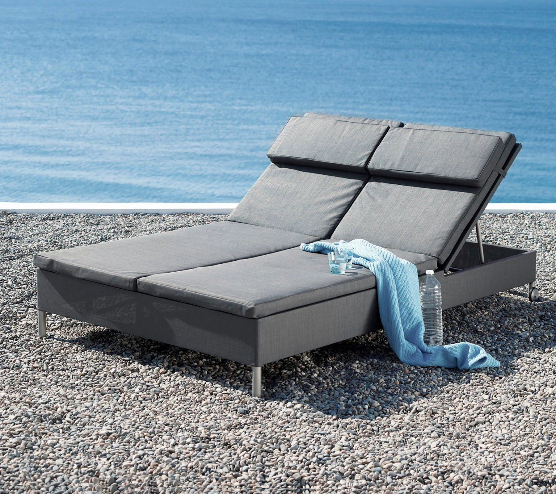   Boxhill's Rest grey outdoor chaise lounge | double sunbed blue fabric and glass of water placed on rocky shore