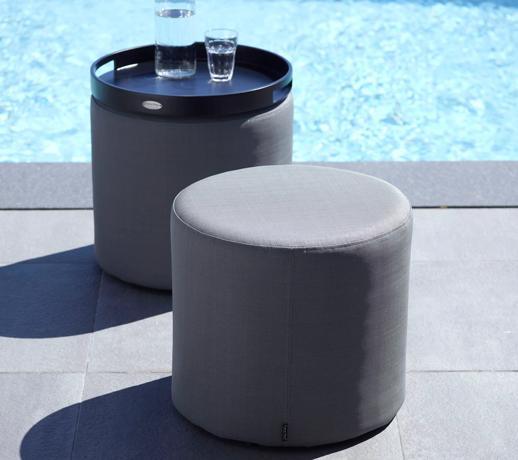  Boxhill's Rest grey outdoor side table | footstool placed on poolside with black round tray and bottle and glass of water on it 