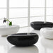 Three glossy oval stone-shaped coffee tables in black and white arranged on a white surface in front of a bright window.