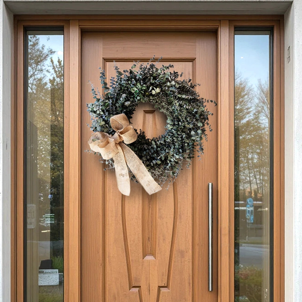 Dried eucalyptus wreath with burlap bow on a wooden front door with glass side panels.