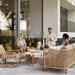 Boxhill's Curve Lounge Weave Outdoor Chair Natural with 2 round tables, 3-seater sofa, 2 women sitting down and a man standing beside