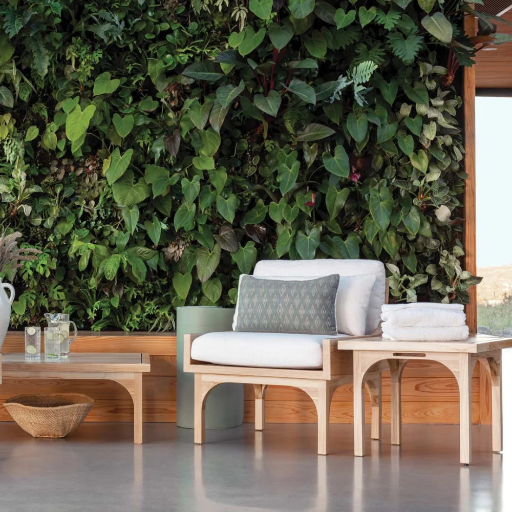 Outdoor seating area with a wooden bench, table, and chairs against a lush green wall.
