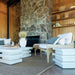 Outdoor living area with stone fireplace, white furniture, and wooden shelves.