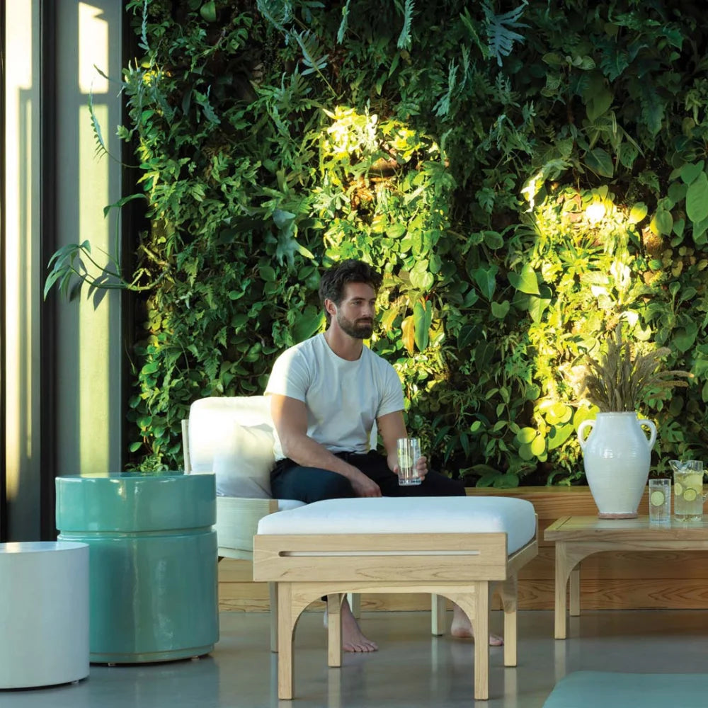 Man sitting on a white outdoor lounge chair in a modern indoor setting with greenery and plants.