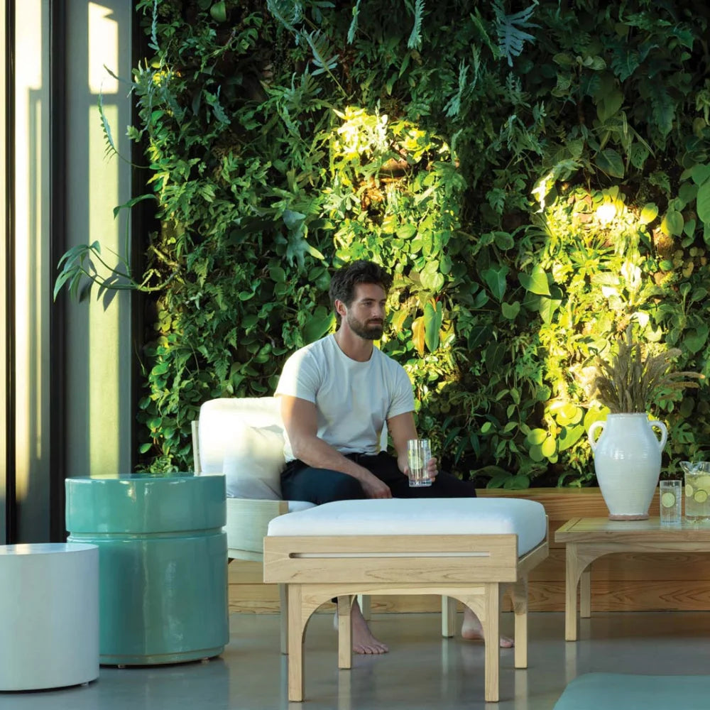 Man sitting on a white outdoor chair in a modern indoor setting with greenery and plants.