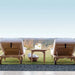 Two wooden outdoor lounge chairs with a small outdoor table and basket on a grassy area with a scenic background.