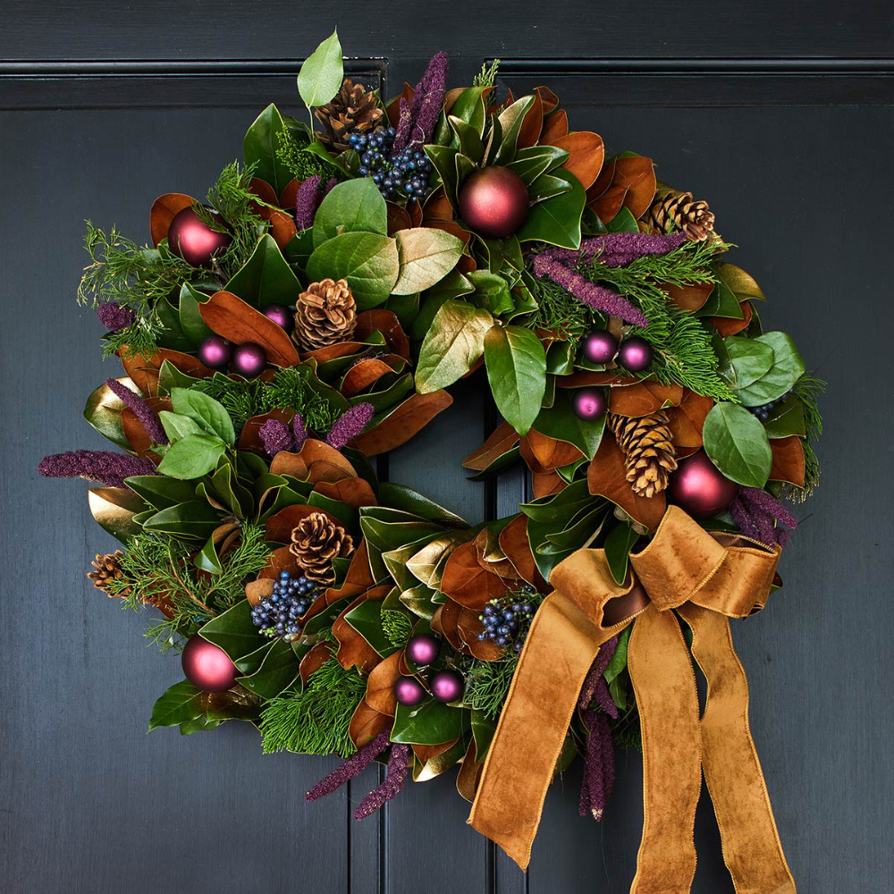 Decorative wreath with greenery, berries, and a brown ribbon on a dark background