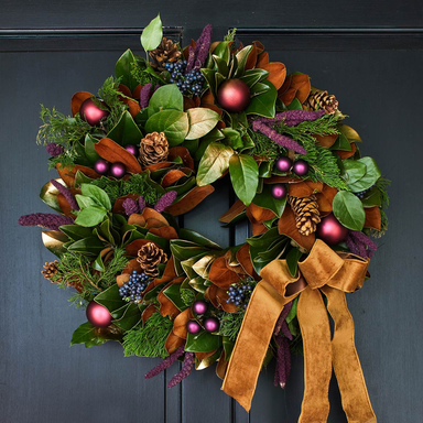 Decorative wreath with greenery, berries, and a brown ribbon on a dark background