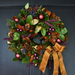 Decorative wreath with greenery, berries, and a brown ribbon on a dark background