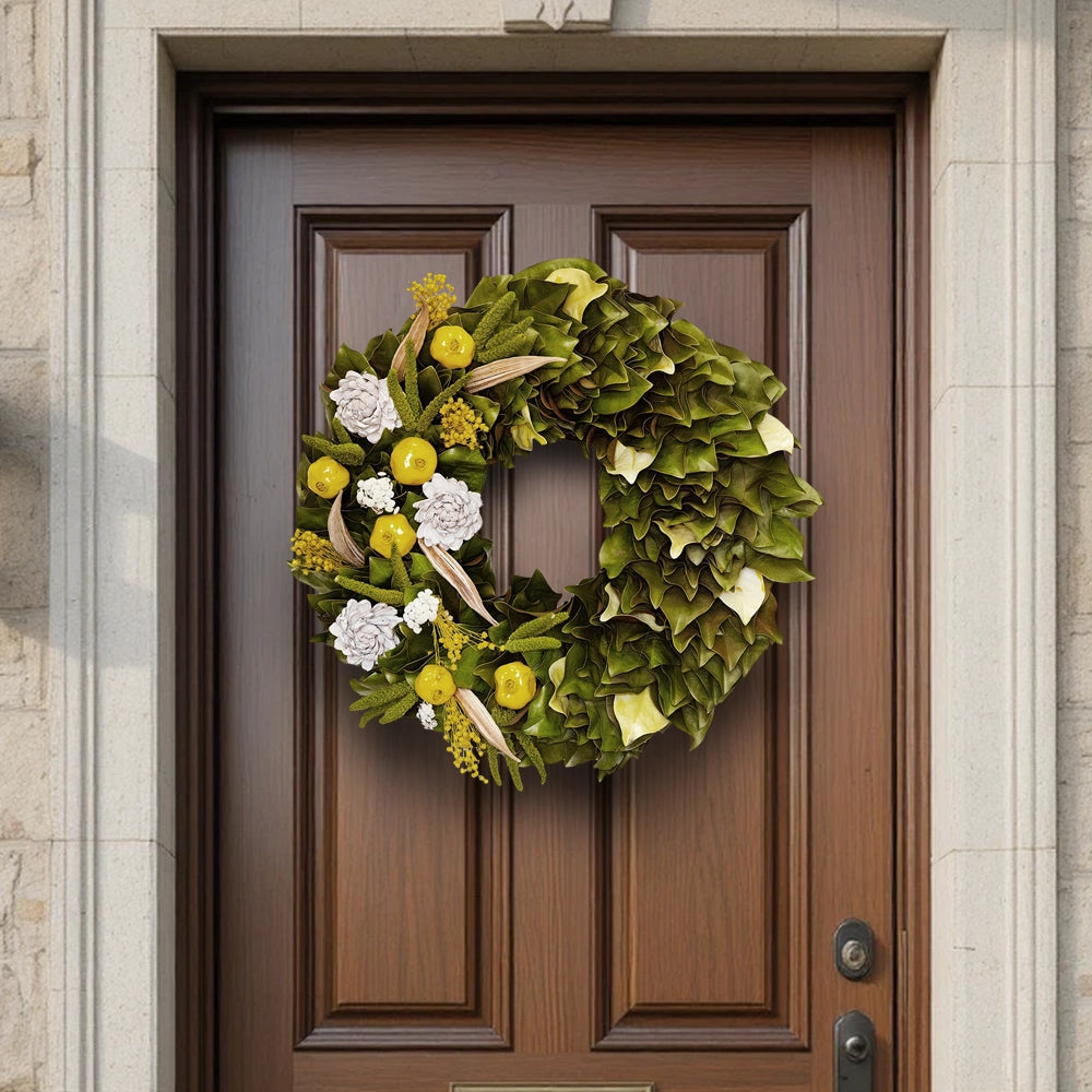 Decorative wreath made of natural and magnolia leaves in yellow-green hues, mounted on a brown wooden front door