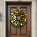 Decorative wreath made of natural and magnolia leaves in yellow-green hues, mounted on a brown wooden front door