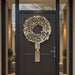 Decorative beige ruffled wreath hanging on a dark modern front door with glass panels.