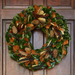 Decorative wreath with green leaves, brown and orange berries, and feathers on a wooden door.